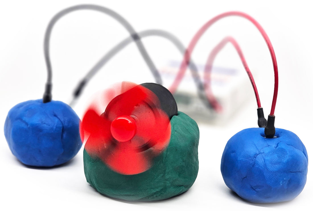 A fan motor spinning on green play dough, wired between two pieces of blue conductive dough
