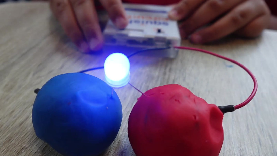 A battery holder wired to a ball of blue dough and a ball of red dough, with an LED glowing across the gap between them