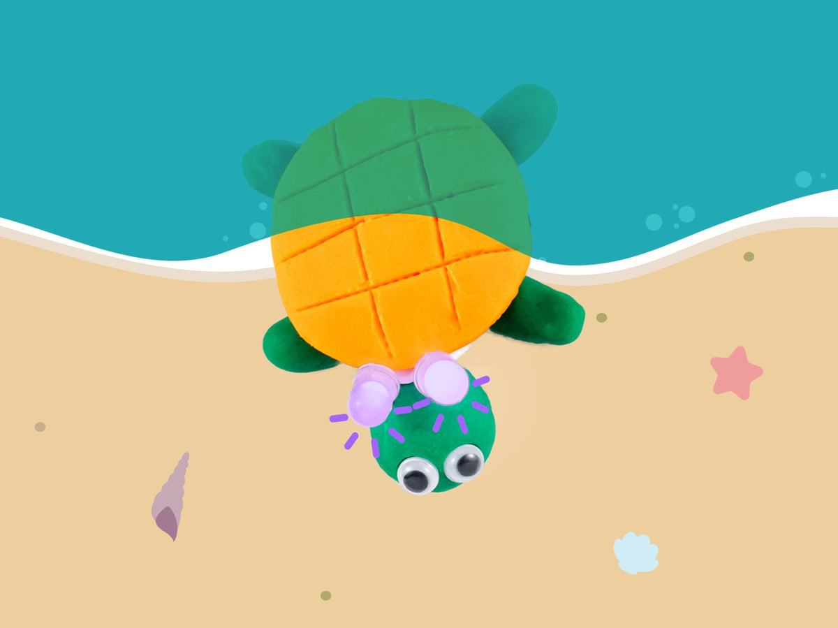 Green dough turtle with an orange shell and googly eyes on a beach