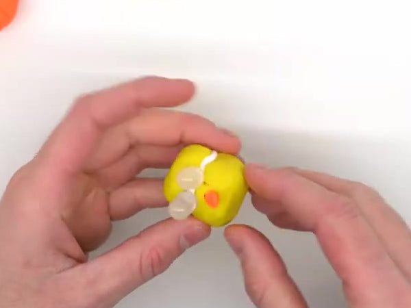 Hands adding a small orange beak to the chick's head