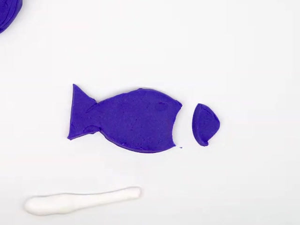 Purple dough fish with its head cut off, next to a rolled strip of white dough