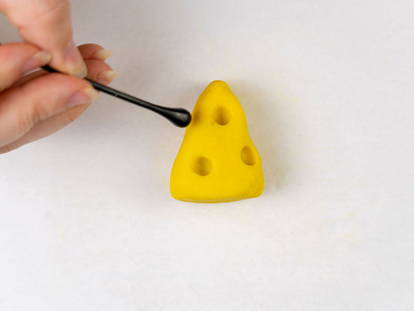 Hand pressing holes into a yellow dough cheese wedge with a tool